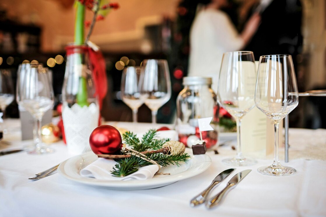 Festlich gedeckter Tisch mit Weihnachtsdeko, Rotwein-Gläsern und Tannenzweigen auf weißer Tischdecke.