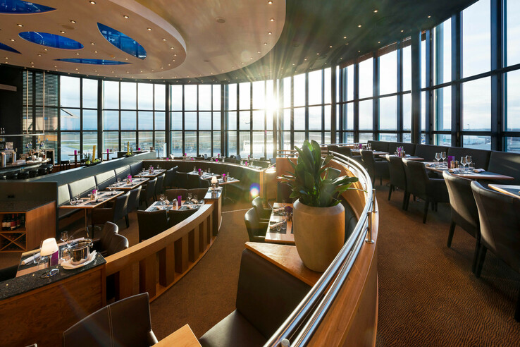 Modernes Restaurant mit Panoramafenstern, elegant gedeckten Tischen und Sonnenuntergang im ATLANTIC Hotel Airport Bremen.