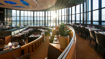 Modernes Restaurant mit Panoramafenstern, elegant gedeckten Tischen und Sonnenuntergang im ATLANTIC Hotel Airport Bremen.