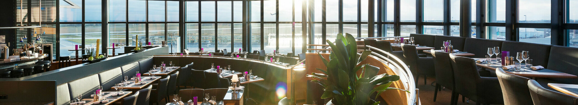 Modern restaurant with panoramic windows, elegantly laid tables and sunset at the ATLANTIC Hotel Airport Bremen.