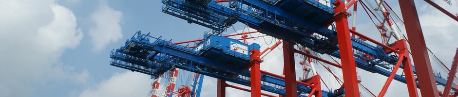Rote und blaue Hafenkräne vor blauem Himmel, bereit zur Containerverladung.