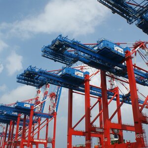 Rote und blaue Hafenkräne vor blauem Himmel, bereit zur Containerverladung.