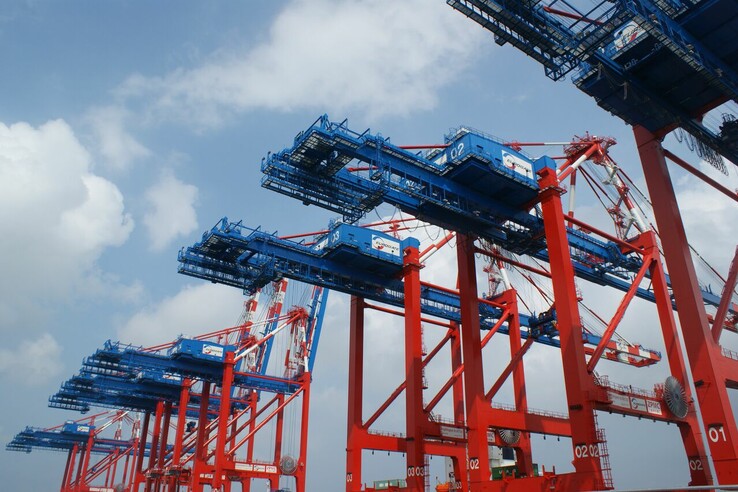 Rote und blaue Hafenkräne vor blauem Himmel, bereit zur Containerverladung.