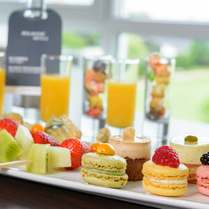 Obstspieße, Macarons und Desserts auf weißem Teller, dahinter Orangensaftgläser im ATLANTIC Hotel Galopprennbahn.