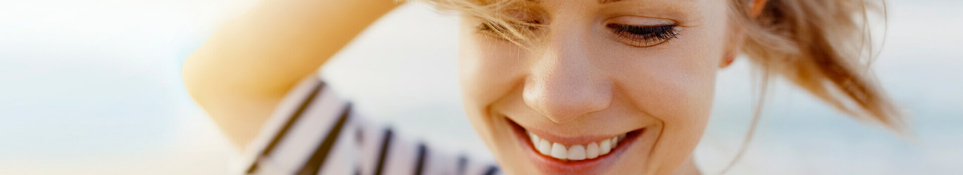 Reopening of the ATLANTIC Hotels Smiling woman on the beach with windblown hair, wearing a striped top.