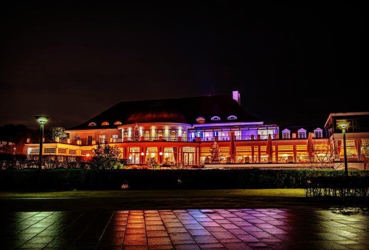 Das ATLANTIC Grand Hotel Travemünde bei Nacht, beleuchtet in warmen Farben, mit reflektierendem Boden im Vordergrund.