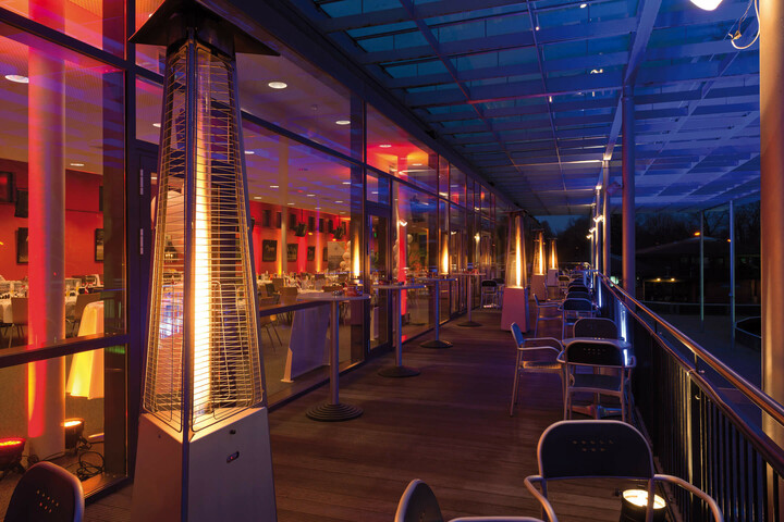fresh air on the balcony of the turflounge Illuminated hotel terrace at night with radiant heaters, tables and chairs, view of the illuminated restaurant.