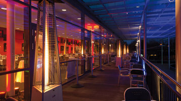 Illuminated hotel terrace at night with radiant heaters, tables and chairs, view of the illuminated restaurant.