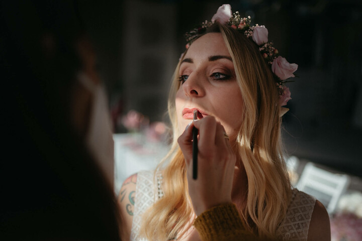Brautstyling vom Atelier "Always & Forever" im ATLANTIC Hotel Münster Eine Frau mit Blumenkranz wird in sanftem Licht geschminkt.