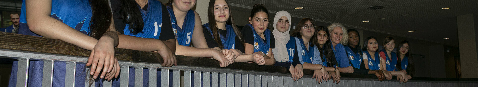 A group of young women in blue jerseys lean against a railing in the ATLANTIC Hotel Sail City.