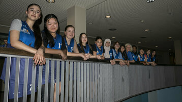 A group of young women in blue jerseys lean against a railing in the ATLANTIC Hotel Sail City.