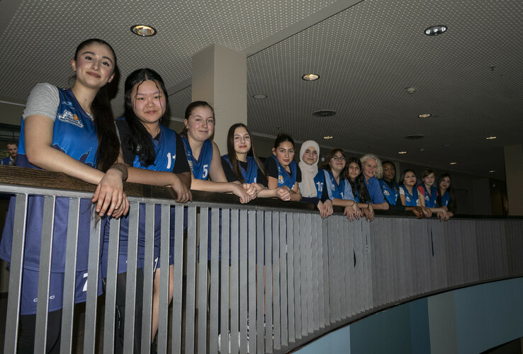 A group of young women in blue jerseys lean against a railing in the ATLANTIC Hotel Sail City.