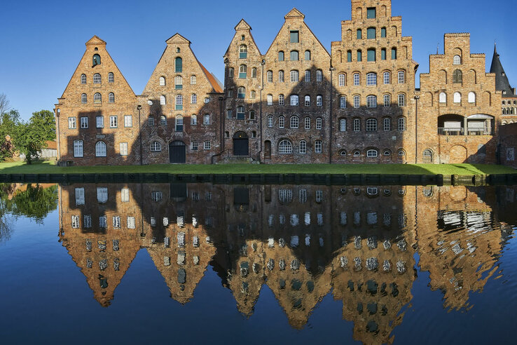 Historische Salzspeicher in Lübeck spiegeln sich im Wasser, klare blaue Himmel im Hintergrund.
