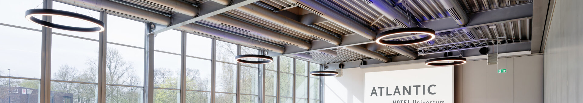 Moderner Konferenzraum im ATLANTIC Hotel Universum mit Tischen, Stühlen und großen Fenstern, die viel Tageslicht hereinlassen.