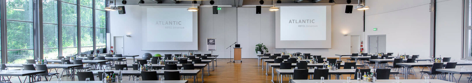Moderner Konferenzraum im ATLANTIC Hotel Universum mit Tischen, Stühlen und großen Fenstern, die viel Tageslicht hereinlassen.
