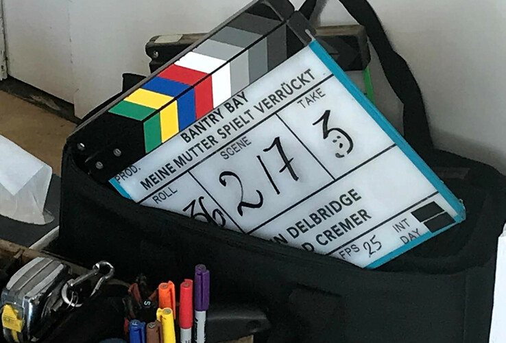 Filmklappe mit der Aufschrift „Meine Mutter spielt verrückt“ in einer Tasche, umgeben von Stiften und Zubehör.