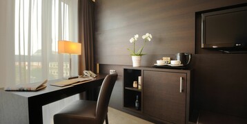 Modernes Hotelzimmer mit Schreibtisch, Lampe, Orchidee, Fernseher und Kaffeemaschine im ATLANTIC Grand Hotel Bremen.