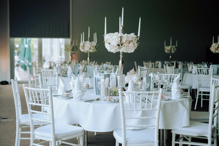 Elegant ballroom with white tablecloths, flower arrangements and candlesticks at the ATLANTIC Hotel Galopprennbahn.