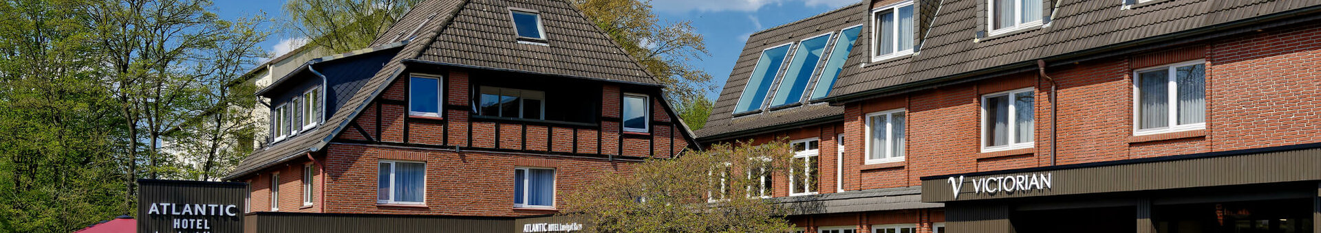 Brick hotel building with pitched roof, parking lot and green surroundings under a blue sky.