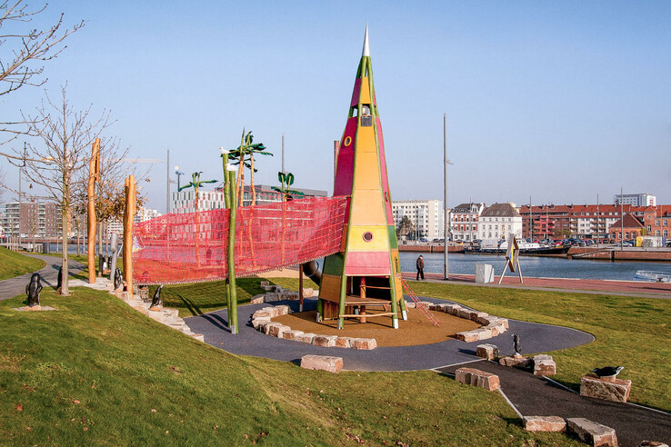 Colorful playground with climbing frame and slide, surrounded by grass, close to the water in an urban environment.
