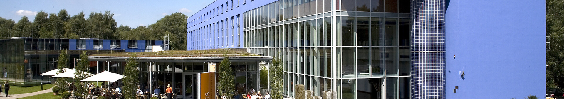 ATLANTIC Hotel Universum in Bremen: Modern, blue building with glass façade, surrounded by green spaces and outdoor seating area.