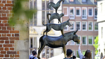 Sculpture of the Bremen Town Musicians in front of a brick façade, people looking at it.