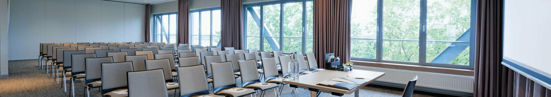 ATLANTIC Hotel Airport Conference Room Bright conference room in the ATLANTIC Hotel Airport Bremen with rows of chairs, table and large windows with a view of the greenery.