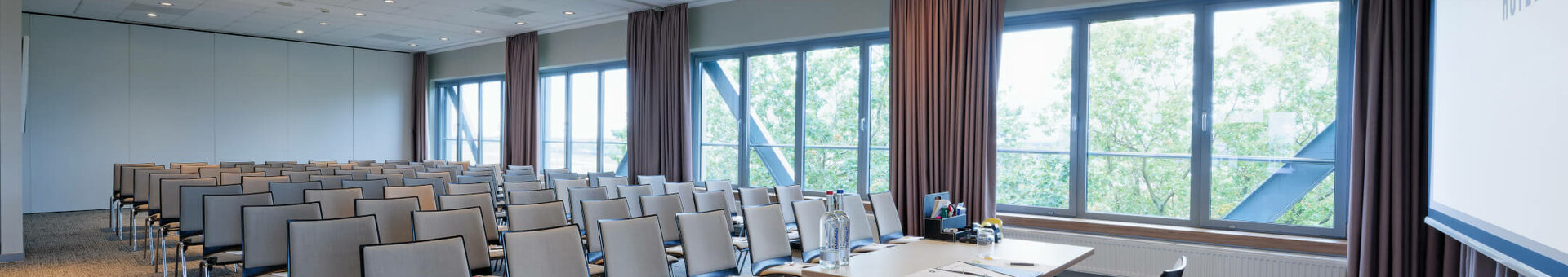 ATLANTIC Hotel Airport Tagungsraum Heller Konferenzraum im ATLANTIC Hotel Airport Bremen mit Stuhlreihen, Tisch und großen Fenstern mit Blick ins Grüne.