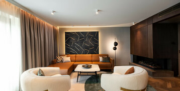 Modernes Hotelzimmer mit braunem Sofa, zwei weißen Sesseln, stilvoller Wandkunst und gemütlichem Kamin.