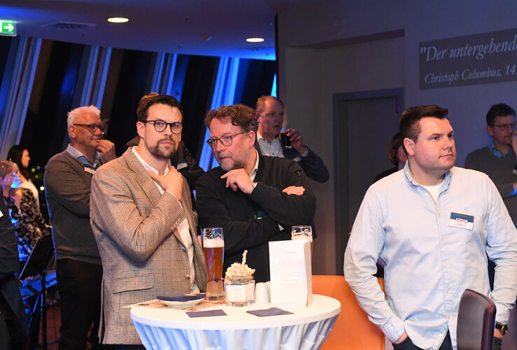 Personen bei einer Veranstaltung im ATLANTIC Hotel Sail City, Bremerhaven, an Stehtisch mit Getränken und Dekoration.