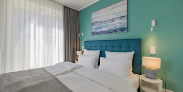 Modern hotel room with a large bed, turquoise wall, maritime picture and soft lighting.