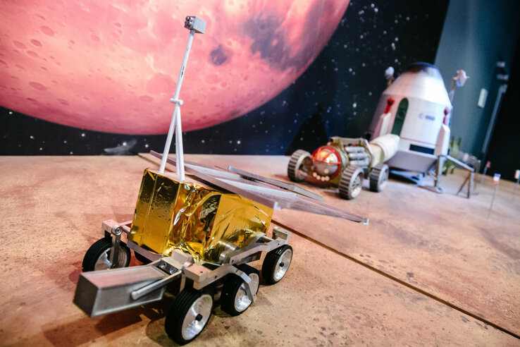 Modell von Mars-Rover und Raumfahrzeug vor einem Mars-Hintergrund in einer Ausstellung.