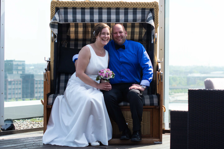 Couple in a beach chair on the terrace of the ATLANTIC Hotel Kiel, laughing, with a bouquet of flowers.