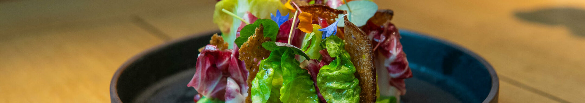 ATLANTIC Hotel Münster Tagungsessen Salat Bunter Salat mit essbaren Blüten und Granatapfelkernen auf dunklem Teller im ATLANTIC Hotel Münster.