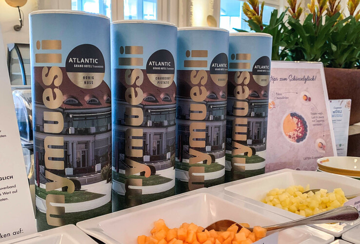 Müslibehälter im ATLANTIC Grand Hotel Travemünde mit frischen Obstwürfeln und Pflanzen im Hintergrund.