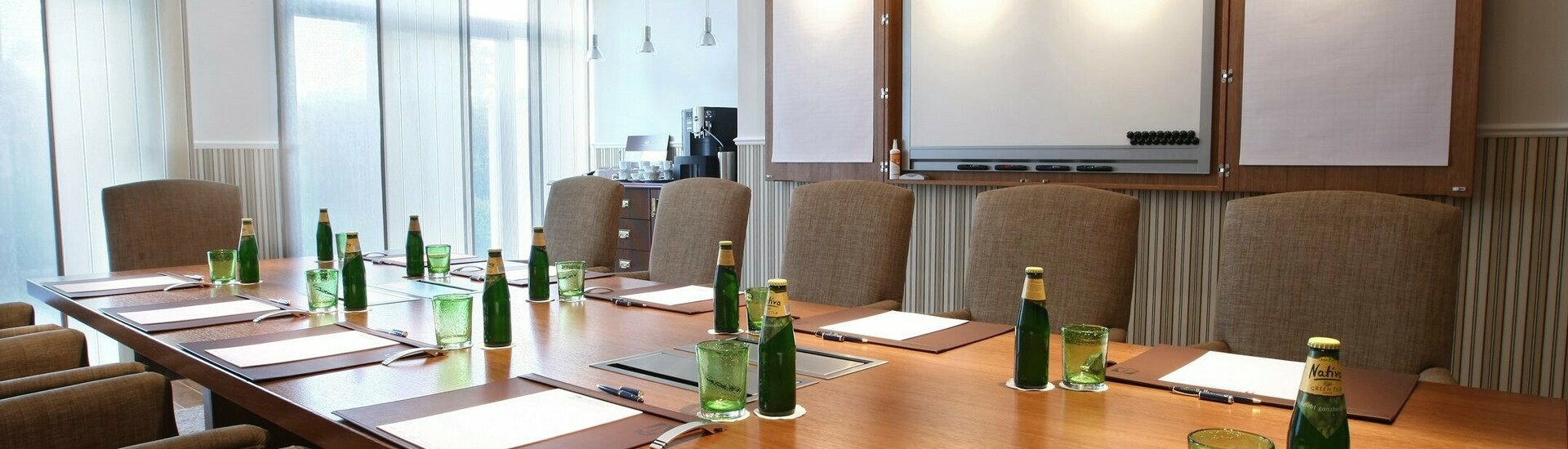 Moderner Konferenzraum im ATLANTIC Grand Hotel Travemünde mit großem Tisch, Stühlen, Flipchart und Getränken.