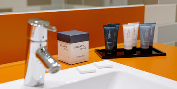 Washbasin with ATLANTIC Hotel care products on an orange background in the bathroom.