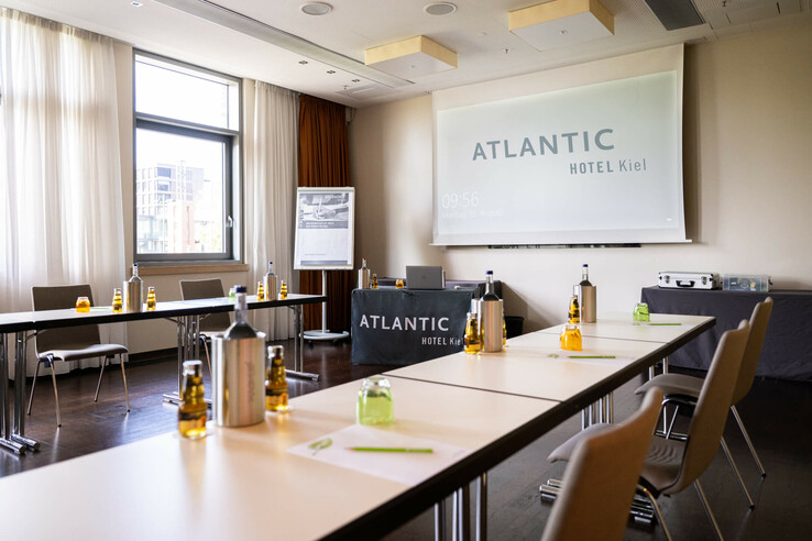 Moderner Konferenzraum im ATLANTIC Hotel Kiel mit Tischen, Stühlen, Getränken und Leinwand.