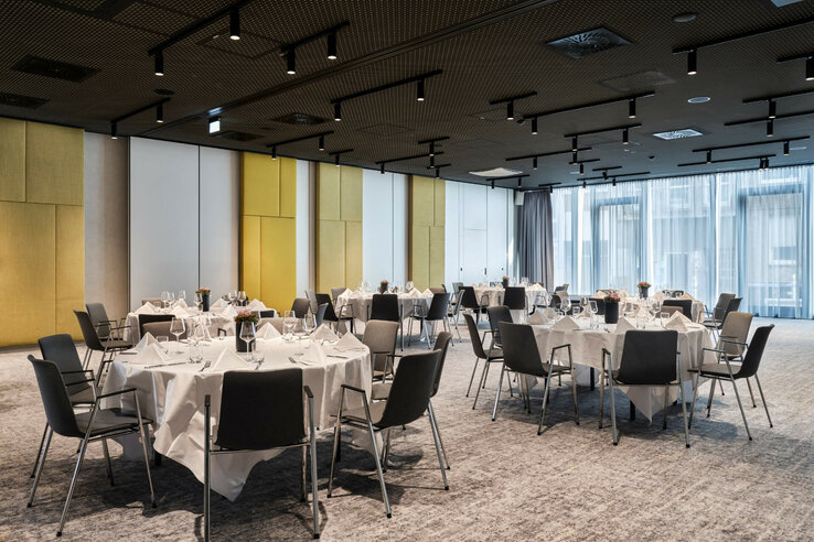 Modern, elegant banquet hall in the ATLANTIC Hotel Münster with round, laid tables and large windows.