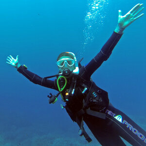 Taucher in voller Ausrüstung unter Wasser mit ausgebreiteten Armen, blauer Hintergrund.