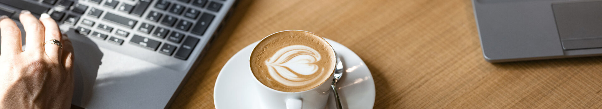 Ein Cappuccino und ein Laptop auf einem Holztisch.