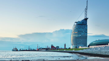ATLANTIC Hotel Sail City in Bremerhaven, modernes Gebäude am Ufer, mit Strand und Meer im Vordergrund.
