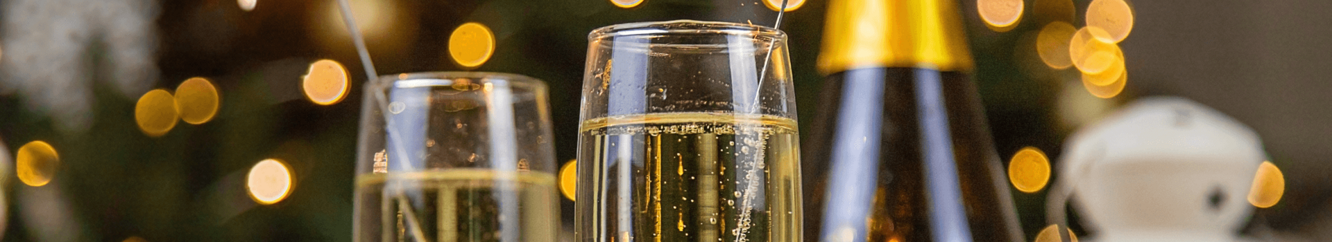 Zwei Sektgläser mit Wunderkerzen, Champagnerflasche und Orangen vor unscharfem, festlichem Hintergrund.