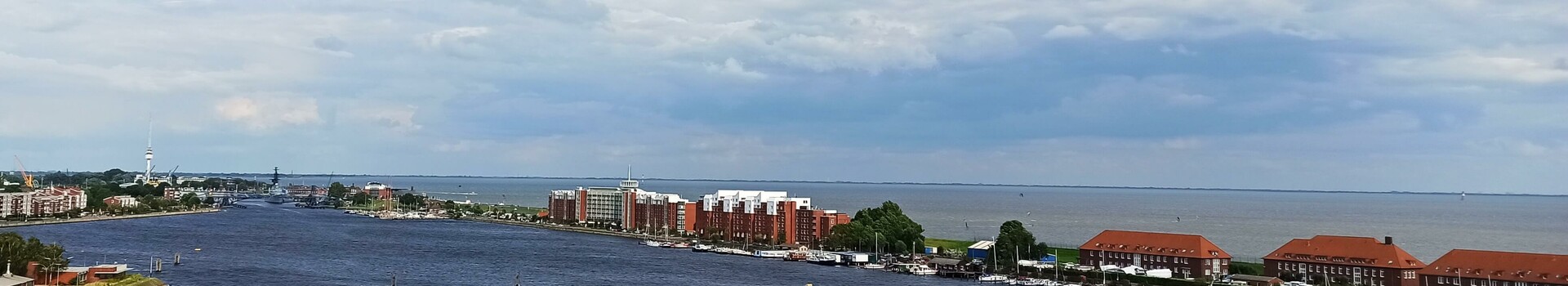 ATLANTIC Hotel Wilhelmshaven - Webcam View of the port of Wilhelmshaven with red brick buildings, water and cloudy sky.
