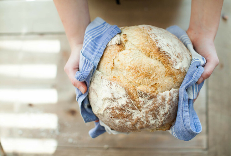 Person holding freshly baked bread in a blue cloth on a wooden table.