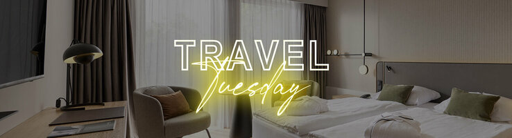 Modern hotel room with two single beds, desk, armchair and large windows with curtains.