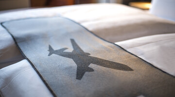 Bed in the ATLANTIC Hotel with gray ceiling, airplane motif, soft lighting.