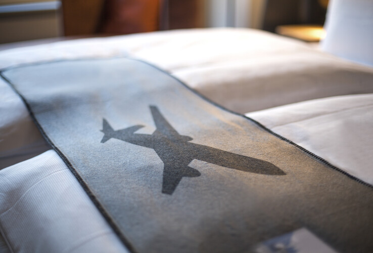 Bed in the ATLANTIC Hotel with gray ceiling, airplane motif, soft lighting.