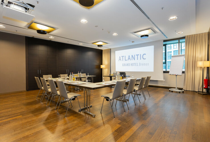 Moderner Konferenzraum im ATLANTIC Grand Hotel Bremen mit Tischen, Stühlen und Präsentationsleinwand.
