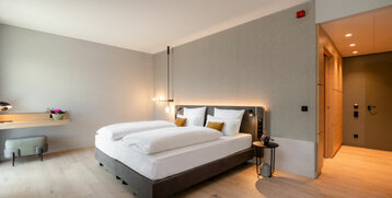 Modernes Hotelzimmer mit Doppelbett, Holzboden, Schreibtisch, Pflanzen und dezenter Beleuchtung im ATLANTIC Hotel Heidelberg.